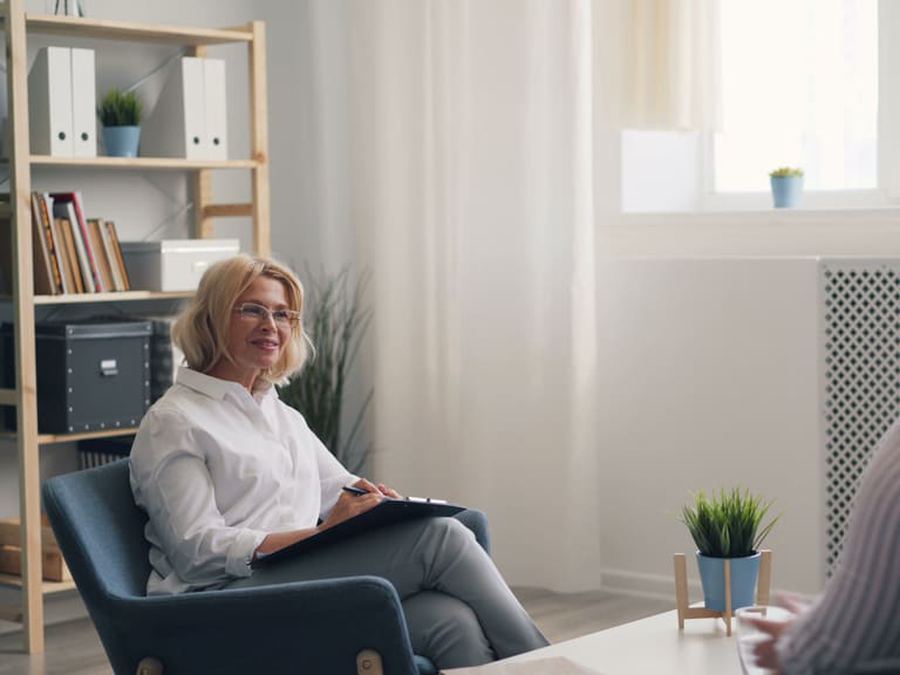 A speech and language therapist with a clipboard listens to a client in a quiet consulting room.